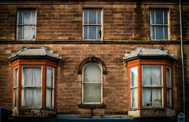 Fototapeta premium Derelict front of old English house, with smashed windows and dirty curtains
