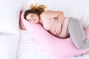 Young pregnant woman with pink pillow sleeping in bed