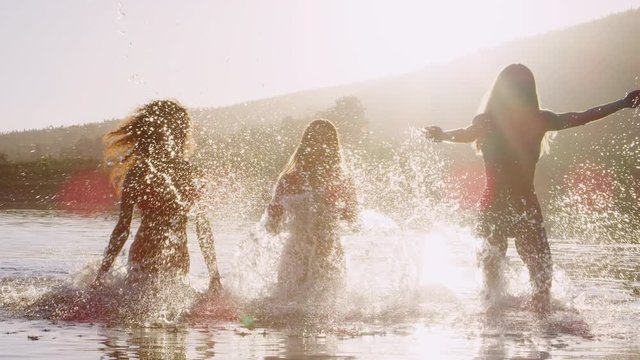 Three female friends running and splashing in a lake
