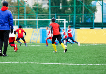 Obraz premium football teams - boys in red, blue, white uniform play soccer on the green field. boys dribbling. dribbling skills. Team game, training, active lifestyle, hobby, sport for kids concept