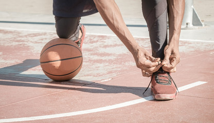 Afroamerican young man playing street basketball in the park is tying his shoes