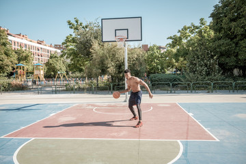 Fototapeta na wymiar Afroamerican young man playing street basketball in the park