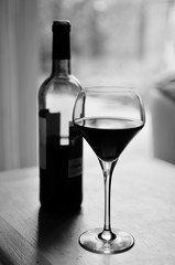 Monochrome wine bottle of red wine and glass on the table in daylight
