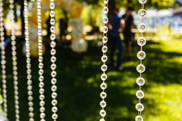 Fragment of creatively decorated wedding arch with hanging glass beads on green background