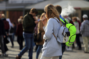 Dziewczyna z plecakiem pali papierosa elektronicznego.