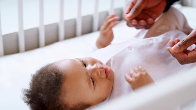 Father Playing With Baby Daughter Lying In Nursery Crib