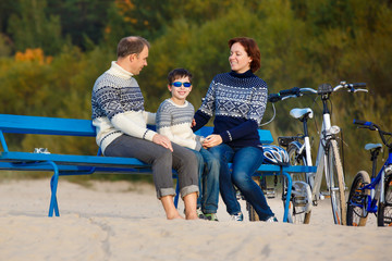 Young family of three having rest on bench during their bike riding on beach
