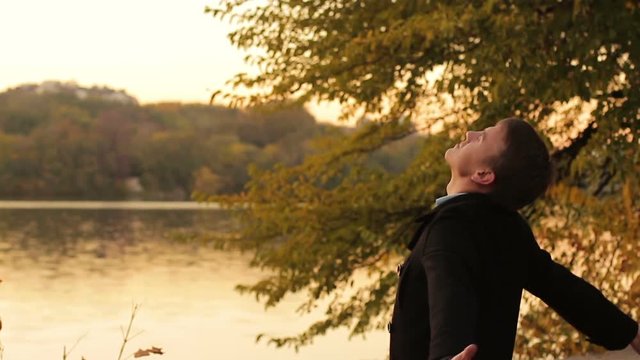 Young man enjoying autumn nature by the river at sunset