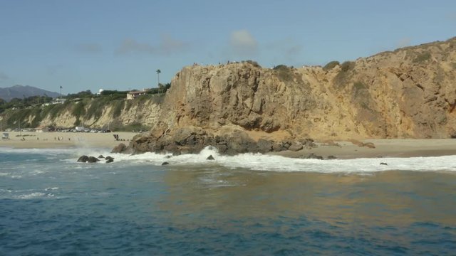 Aerial pullback over the waves and rocks of a cliff on the beach.