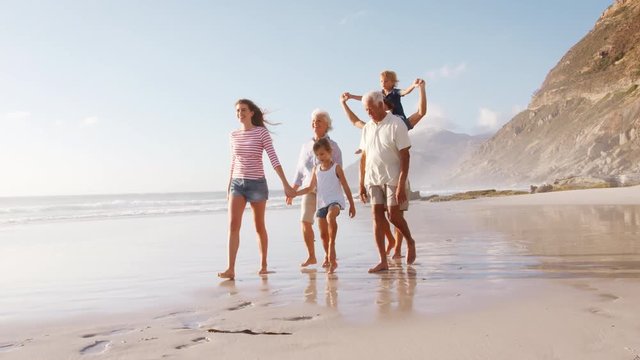 Multi Generation Family On Summer Vacation Walking Along Beach