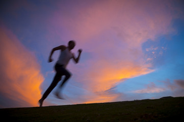 Fototapeta na wymiar Motion blur silhouette of man running against vibrant sunrise sky