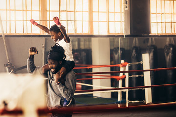 Kid sitting on shoulders of boxing coach celebrating a win