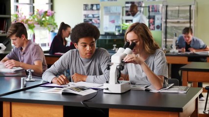 High School Students With Tutor Using Microscope In Biology Class - Powered by Adobe