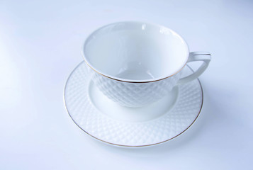 One empty tea set: white porcelain with gold textured cup and a plate at white background. High resolution