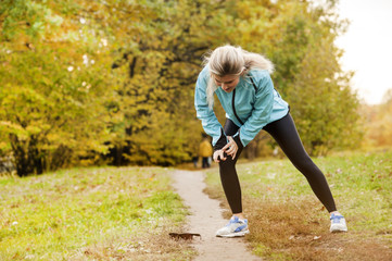 the athlete has a sore knee while jogging, and he stands in pain and massages his sore knee in a park in the fall