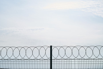 Barbed wire against cloudy sky, close-up. Metal fence with barbed wire, outdoors 