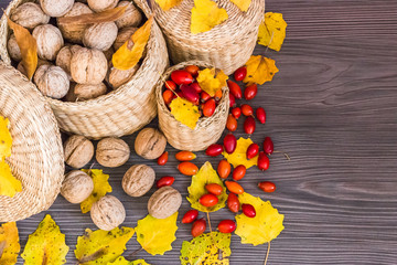 Walnuts, rose hips and yellow leaves on a wooden surface, healthy food from nature. Concept of autumn background