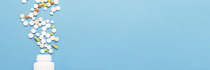 White bottle and multi-colored pills on a blue background. Concept of pharmaceuticals, medicine,...