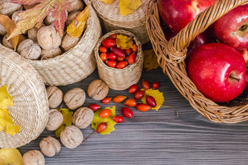 Walnuts, red apples in basket, rose hips and yellow leaves on a wooden surface, healthy food from nature. Concept of autumn background