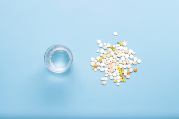 Glass of water and various pills on a blue background. The concept of taking drugs in case of illness and disease. Flat lay, top view