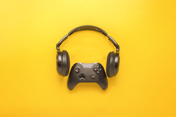 Black headphones and a gamepad on yellow background. Concept of the game on the console or...