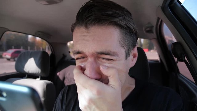 Sad desperate man reading bad sms at smatphone crying in the car