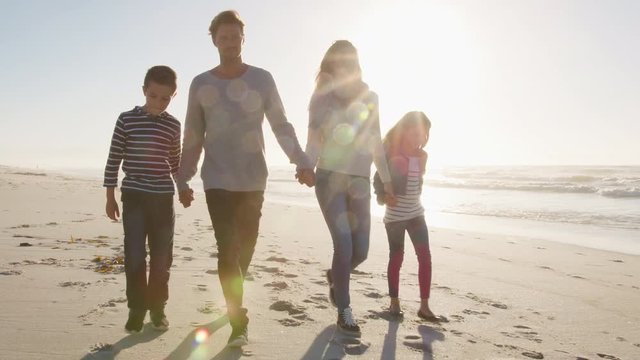 Family Walking On Winter Beach Holding Hands With Flaring Sun