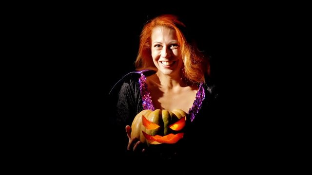 Beautiful girl with red hair laughs and holds a pumpkin in the hands in the dark