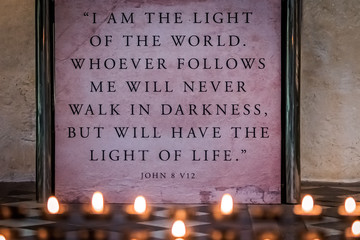 Memorial candles burning in front of a wall plaque with bible verse