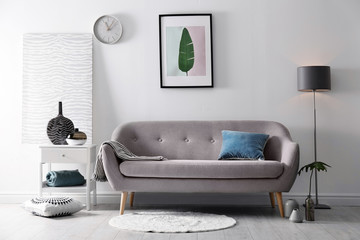 Living room interior with vases on side table and comfortable sofa near white wall