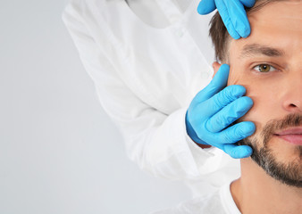 Doctor examining mature man face before cosmetic surgery on white background, closeup