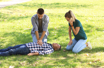 Passersby helping unconscious man outdoors. First aid