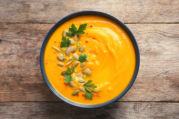 Delicious pumpkin cream soup in bowl on wooden background, top view