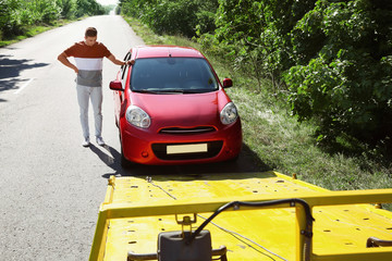 Man near broken car and tow truck on country road