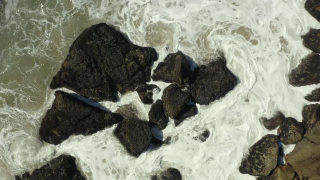 Birdseye view of waves crashing against rocks on the beach.