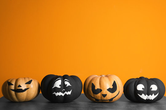 Pumpkins with scary faces on table against color background, space for text. Halloween decor