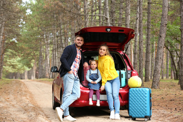 Happy young family near car trunk loaded with suitcases outdoors