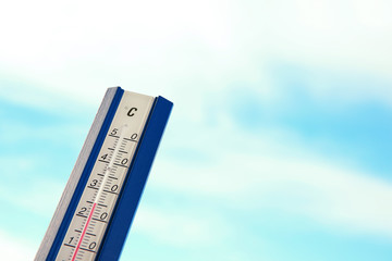 Weather thermometer and blue cloudy sky on background. Space for text