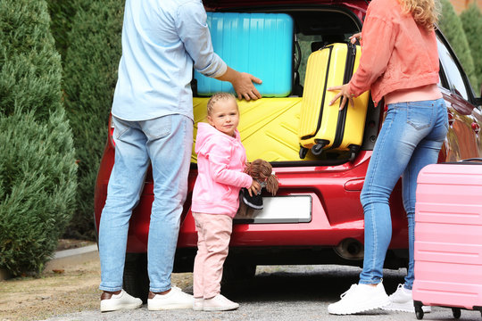 Young family loading suitcases in car trunk outdoors