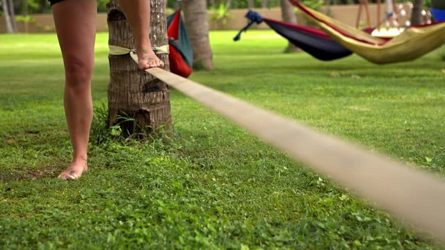 Girl walking on the sling. Young woman balancing on slackline at a beach between palm trees. Lady practice in balance balancing on one leg. Active and health life. Fitness sport and lifestyle concept.