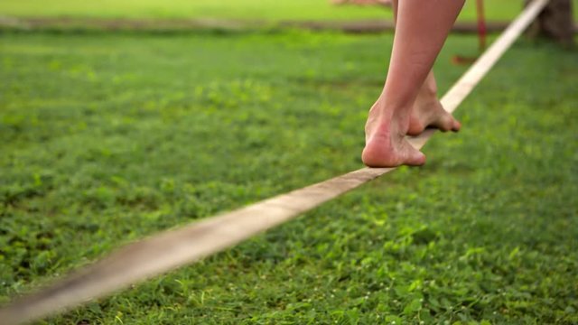 Girl walking on the sling. Young woman balancing on slackline at a beach between palm trees. Lady practice in balance balancing on one leg. Active and health life. Fitness sport and lifestyle concept.