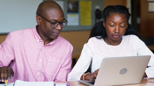 High School Tutor Giving Female Student Using Laptop One To One Tuition At Desk