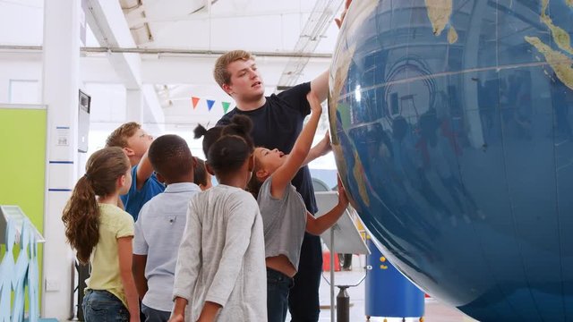 School kids using giant globe with teacher at science centre