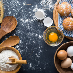 Baking ingredients. Bowl, eggs, flour, eggbeater, rolling pin and eggshells on black chalkboard from above.