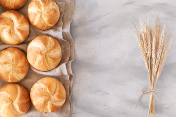 Crusty round bread rolls, known as Kaiser or Vienna rolls with a bunch of wheat ears on light...