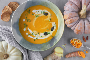 Pumpkin creme soup in ceramic bowl seasoned with thyme, cream and croutons, with pumpkin, chili pepper and fresh curcuma
