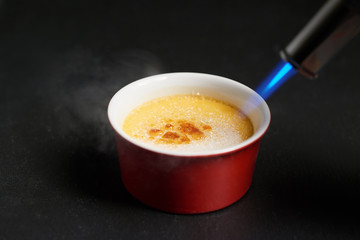 Caramelising sugar on top of creme brulee with flaming torch on dark