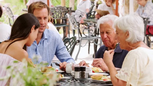 Young adult and senior couple eating together outside a cafe