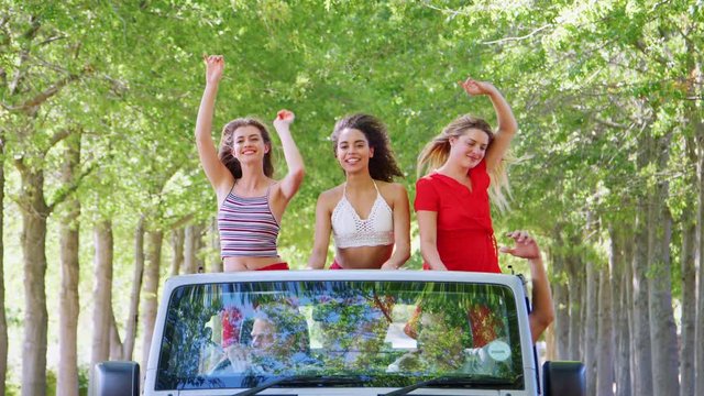 Girlfriends standing in the back of an open top car dancing