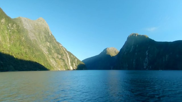 wide shot of the first sunbeams during sunrise hitting the cliffs of the mountains in a fiord, Milford Sound, New Zealand